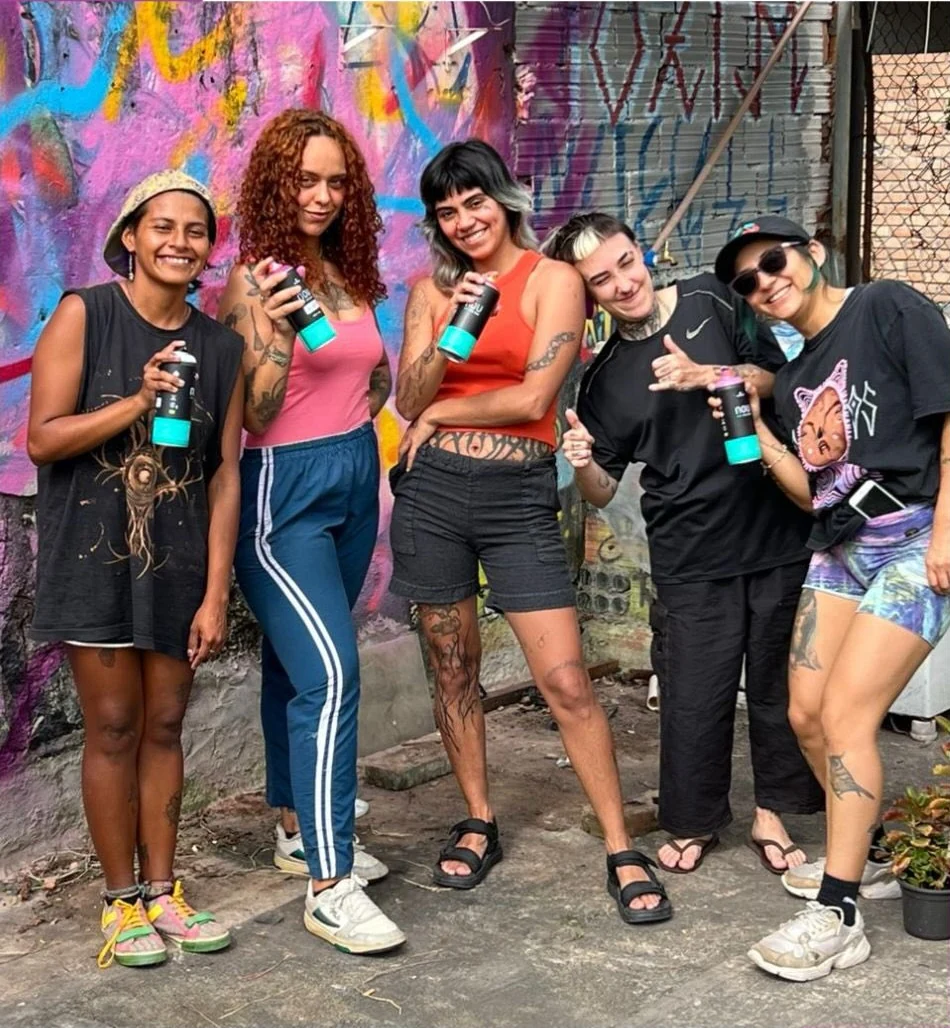 Grupo de mulheres com latas de spray diante de parede pintada